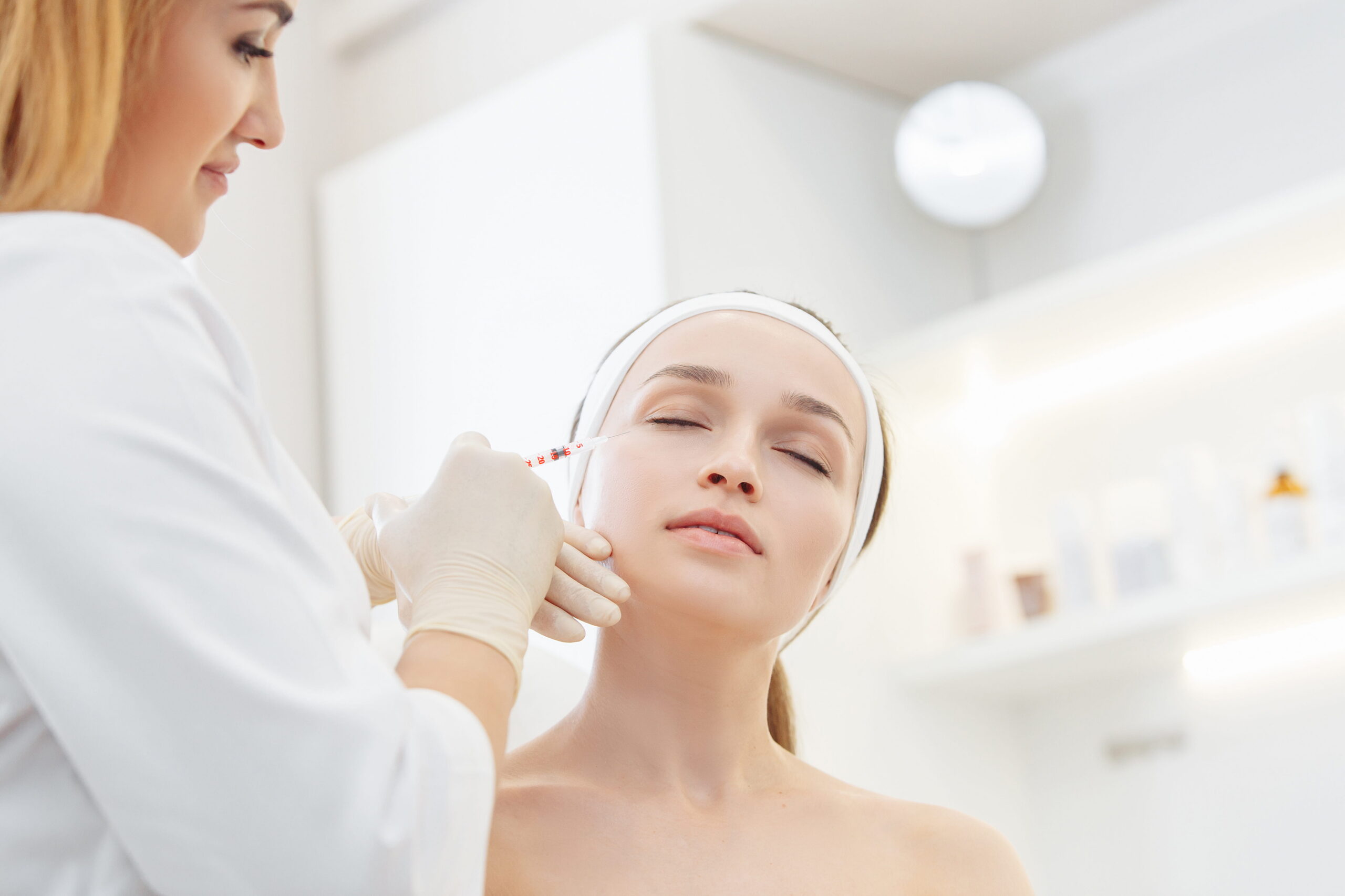 master cosmetologist makes botox injections into the eyebrow of a beautiful young woman